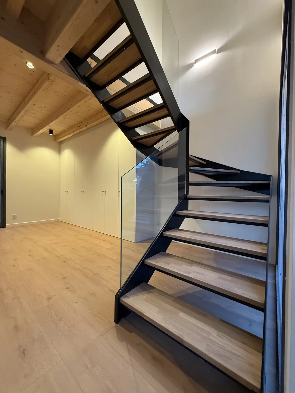 Escalera MANI FRAME: estructura negra, peldaños de madera y barandilla de cristal